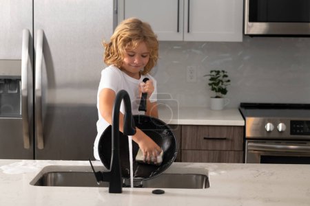 Photo for Home chores. Kid in kitchen cleaning plates. Cute boy washing dishes in domestic kitchen. Child housekeeper washing the dishes on soapy water. Cute Funny boy washing dishes in kitchen - Royalty Free Image
