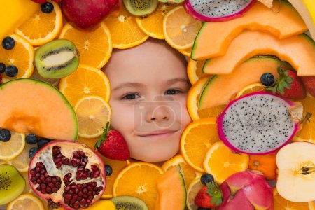 Téléchargez les photos : Funny fruits. Kid smiling face portrait surrounded by fruits. Kids face are peeking out of the mix fruits - en image libre de droit