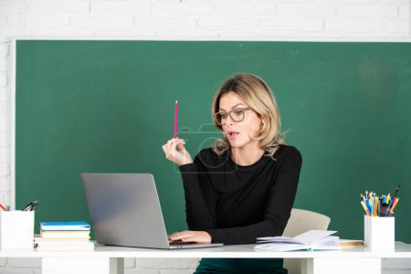 Téléchargez les photos : Modern attractive teacher. Portrait of smart young woman in glasses with book on the blackboard in class at high school or collage. Female professor at school, ready to start lesson - en image libre de droit