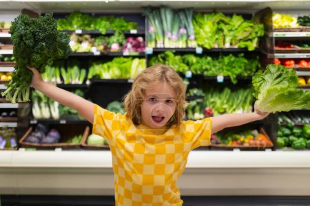 Téléchargez les photos : Child with lettuce chard vegetables. Kid on shopping in supermarket. Grocery store, choosing goods. Shopping for healthy - en image libre de droit