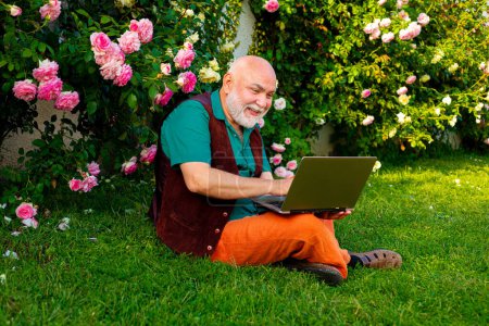 Téléchargez les photos : Elderly pensioner enjoy his retirement. Happy senior in using laptop on backyard. Retirement lifestyle - en image libre de droit