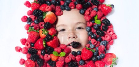 Téléchargez les photos : Berrie set. Child face with berry frame, close up. Berries mix blueberry, raspberry, strawberry, blackberry. Assorted mix of strawberry, blueberry, raspberry, blackberry near child face - en image libre de droit