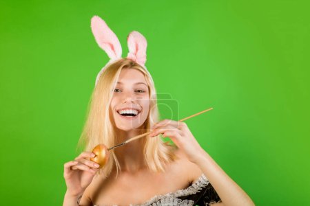 Téléchargez les photos : Joyeux jeune femme peignant des œufs. Des gens heureux. Souriez Pâques. Belle blonde sensuelle. Superbe belle jeune fille dans les oreilles de lièvre souriant dessin d'un oeuf de Pâques - en image libre de droit