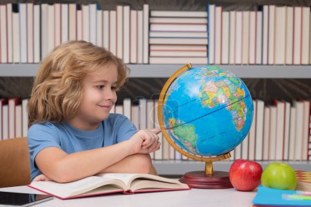 Foto de School kid pupil looking at globe in library at the elementary school. World globe. School kid 7-8 years old with book go back to school. Little student. Education concept - Imagen libre de derechos