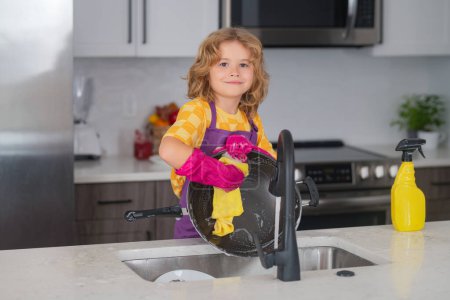 Foto de Housekeeping, home chores. Kid housekeeper. Child washing and wiping dishes in kitchen. American kid learning domestic chores at home. Housekeeping children concept - Imagen libre de derechos