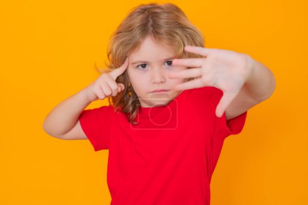 Téléchargez les photos : Child in red t-shirt making stop gesture on isolated studio background. Kid showing warning symbol, hand sign no. Kids protection, bullying, abuse and violence concept - en image libre de droit
