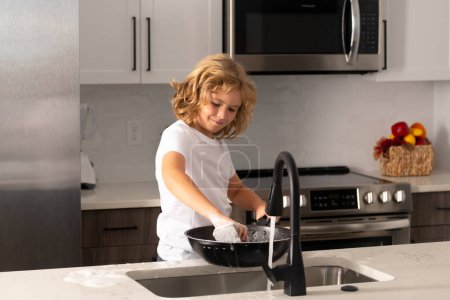 Téléchargez les photos : Child housekeeper washing the dishes on soapy water - en image libre de droit