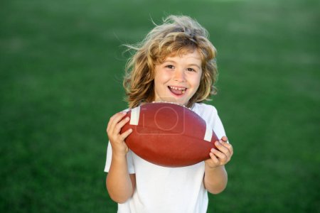 Téléchargez les photos : Outdoor kids sport activities. Kids and sports. Young boy playing american football. Child holding rugby ball while playing american football in Summer park - en image libre de droit