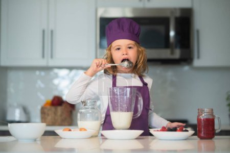 Photo for Chef child cooking healthy meal and dinner preparation. Kids are preparing the dough, bake cookies in the kitchen, lick spoon - Royalty Free Image