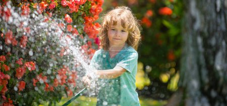 Téléchargez les photos : Spring child watering, banner. Child watering flowers and plants in garden. Kid with water hose in backyard. Kids gardening. Kids summer fun outdoor at home - en image libre de droit