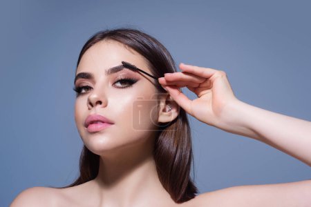 Photo for Eyebrow shaping, woman combs eyebrows with a brus. Eyebrow line. Makeup and cosmetology concept. Female model with long eyelashes and thick eyebrows. Perfect shaped brow - Royalty Free Image