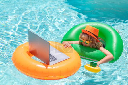 Téléchargez les photos : Child swimming on an inflatable ring with a laptop water pool. Shopping online, freelance concept, summer travel - en image libre de droit