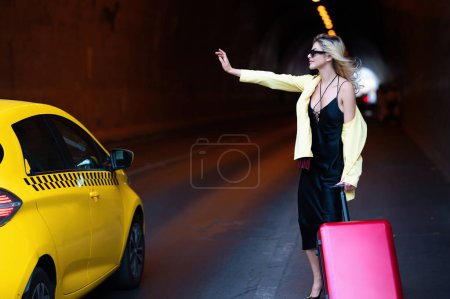 Foto de Travelling concept. Woman with a suitcase take taxi. Sexy young woman on trip walking with his luggage on street. Sensual girl with travel bag ready to travel on vacation - Imagen libre de derechos