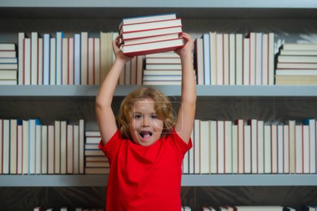 Foto de Amazed school kid hold stack of books. Excited amazed school boy. Knowledge and education school concept. School boy pupil reading book in library. Kids learn to read - Imagen libre de derechos