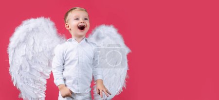 Téléchargez les photos : Valentines day banner with angel child. Portrait of happy smiling little curly blond Angel boy. Angelic child. Toddler wearing angel white dress costume and feather wings. Consept of innocent child - en image libre de droit