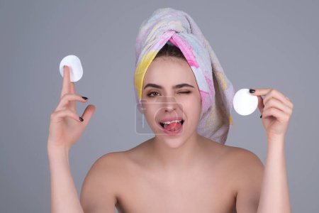 Téléchargez les photos : Beautiful young woman with cotton pad, applying lotion on face, removing makeup. Skin care. Studio portrait of girl cleaning her face with cotton pad, isolated background. Face toner and cotton pad - en image libre de droit