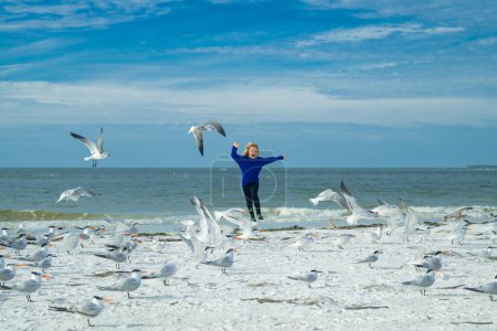Téléchargez les photos : Bonne enfance. Enfant garçon chassant les oiseaux près de la plage de la mer d'été. Enfant heureux jouant avec les oiseaux de mouette dehors le jour d'été - en image libre de droit