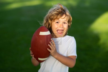 Téléchargez les photos : Enfant sportif. Enfant avec football américain, ballon de rugby. Portrait mignon d'un footballeur américain - en image libre de droit