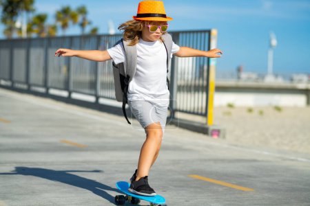 Téléchargez les photos : Boy on skateboard skating. Kid boy riding skateboard in the road. Kid practicing skateboard. Children learn to ride skateboard in a park on sunny summer day - en image libre de droit