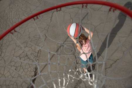 Foto de Lindo niño sonriente juega con la pelota de cesta. Lindo niño pequeño en uniforme de baloncesto saltando con pelota de baloncesto para el tiro. Deporte para niños - Imagen libre de derechos