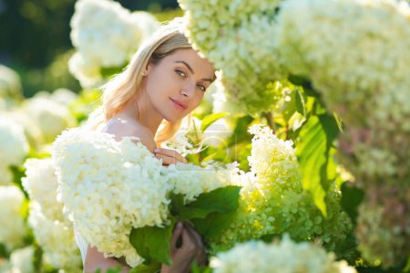 Foto de Lovely girl standing on soft background hydrangea blossoming flowers, tenderness. Portrait of a very beautiful sensual and sexy girl in the summer garden on a background of hydrangea flowers - Imagen libre de derechos