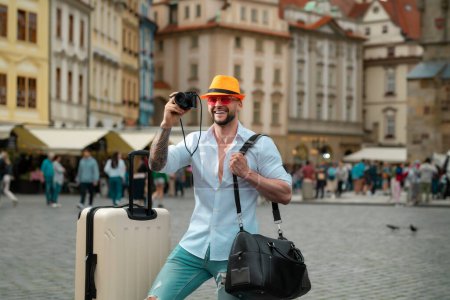 Foto de Turista caminando por la calle de la ciudad. Hombre viajero con gafas de sol, sombrero y cámara. Hombre con bolsa de viaje listo para viajar en sus vacaciones - Imagen libre de derechos