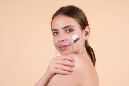 Photo for Beauty portrait of a beautiful half naked woman applying face cream isolated on studio background. Skin care product. Moisturizing creme on face. Perfect skin, morning routine - Royalty Free Image