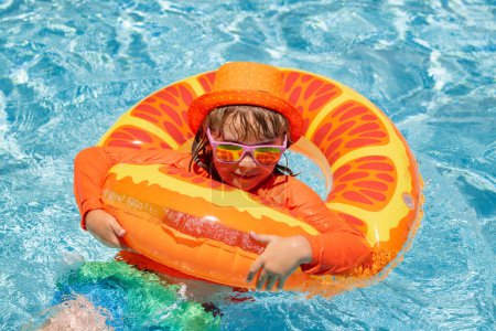 Foto de Kid boy swimming in pool play with floating ring. Smiling cute kid in sunglasses swim with inflatable rings in pool in summer day - Imagen libre de derechos