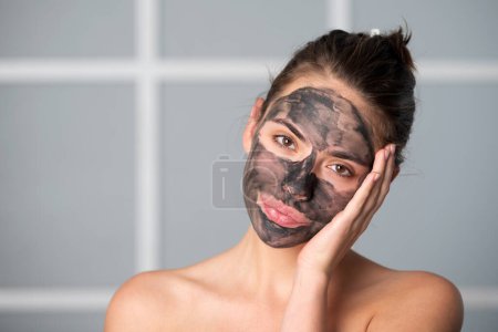 Téléchargez les photos : Femme avec masque de boue faciale au fusain sur le visage. Procédure cosmétique. Spa de beauté et cosmétologie. Spa femme appliquant gris masque d'argile faciale. Soins de beauté - en image libre de droit