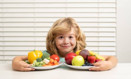 Téléchargez les photos : Fruits et légumes. Un gamin qui mange des légumes sains. Petit déjeuner avec lait, fruits et légumes. Manger des enfants pendant le déjeuner ou le dîner - en image libre de droit