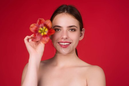 Photo for Beauty girl with tulip near face. Youth and skin care concept. Beautiful sensual woman hold tulips, studio portrait on red background - Royalty Free Image