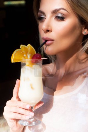 Téléchargez les photos : Modèle de mode dans une tenue d'été élégante profitant d'un cocktail, tenant un cocktail d'alcool savoureux décoré avec des fraises. Femme sexy boire pina colada cocktail en été et profiter de ses vacances - en image libre de droit