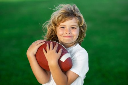 Téléchargez les photos : Activités sportives pour enfants en plein air. Enfant avec football américain, ballon de rugby. Portrait mignon d'un footballeur américain - en image libre de droit