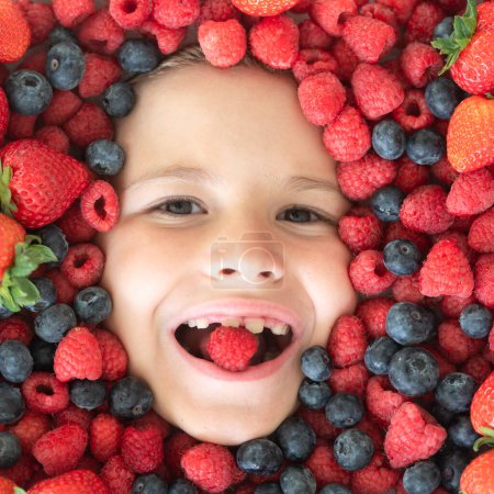 Téléchargez les photos : Une saine alimentation. Visage d'enfant avec baies en gros plan. Mélange de fraises, bleuets, framboises, mûres. Mélange assorti de fraise, myrtille, framboise, mûre avec fond près du visage de l'enfant - en image libre de droit