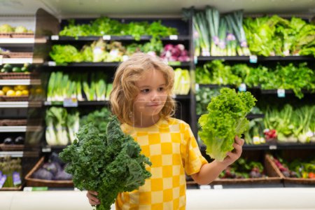 Téléchargez les photos : Enfant avec des légumes à la laitue. Shopping au supermarché. Les enfants achètent des courses au supermarché. Le petit garçon achète des légumes frais à l'épicerie. Enfant dans le magasin - en image libre de droit