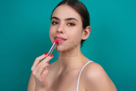 Photo for Model girl holding lipstick over color studio Background. Beauty woman face, cosmetics make up. Fashion model applying lip gloss makeup. Sexy woman applying lipstick on lips - Royalty Free Image