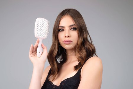 Téléchargez les photos : Studio portrait of attractive pretty haired girl combing hair. Hair care, hairs salon. Beautiful woman with healthy skin straight hair isolated on studio background. Hairs day. Beautiful smooth hair - en image libre de droit