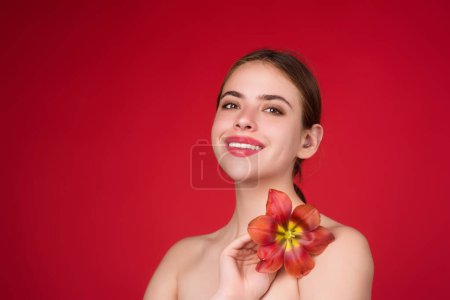Foto de Chica de belleza con tulipán cerca del hombro desnudo. Hermosa mujer sensual mantenga tulipanes, retrato de estudio sobre fondo rojo - Imagen libre de derechos