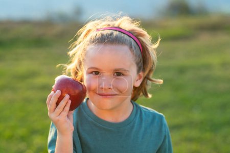 Foto de Apple child. Child bites big apple, against green summer garden - Imagen libre de derechos