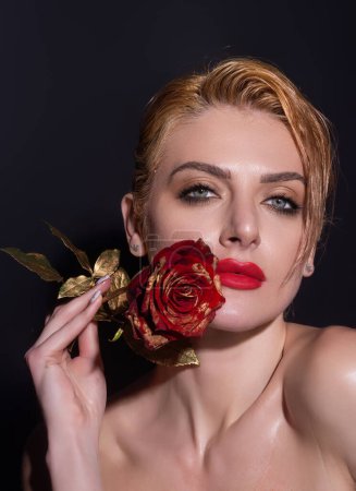 Foto de Retrato de estudio de belleza. Hermoso modelo con flor de rosa roja, aislado sobre fondo de estudio negro. Encantadora joven con maquillaje perfecto - Imagen libre de derechos