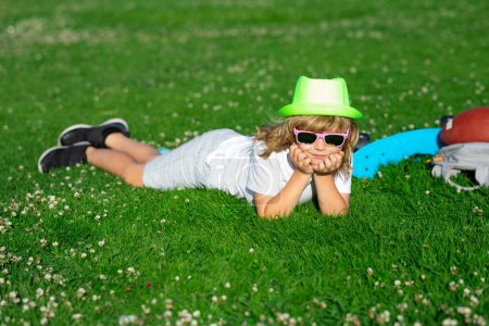 Téléchargez les photos : Cute child boy enjoy relax on lawn. Kids relaxation. Child laying in grass in the park. Summer holiday activitie. Kid boy are relaxing outdoor. Child playing in the garden - en image libre de droit