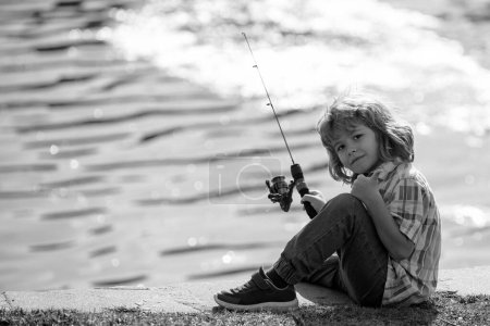 Téléchargez les photos : Un jeune pêcheur à River. Pêche pour enfants, activités de plein air estivales. Petit garçon pêchant au bord de la rivière avec canne - en image libre de droit