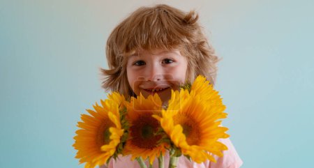Téléchargez les photos : Enfant souriant avec des tournesols. Joyeux enfant avec bouquet de fleurs. mignon charmant garçon romantique et surprise - en image libre de droit