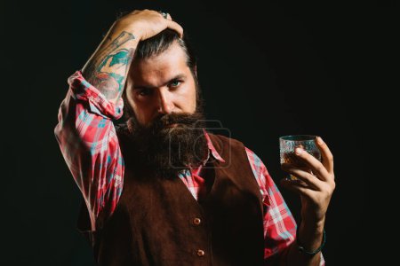 Foto de Empresario barbudo en traje elegante con vaso de whisky. Bebiendo whisky. Hombre guapo barbudo sosteniendo un vaso de whisky - Imagen libre de derechos