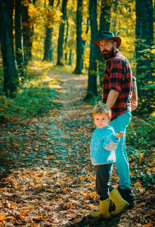 Photo for Happy kid wearing warm clothes relaxing with parent in autumn. Outdoors activities. Father walks with his son by autumnal forest path. Bearded dad in hat have fun with little child - Royalty Free Image