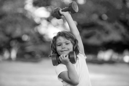 Téléchargez les photos : Fitness haltères enfant séance d'entraînement d'exercice en plein air. Garçon enfant sportif avec haltères. Activités saines mode de vie des enfants - en image libre de droit