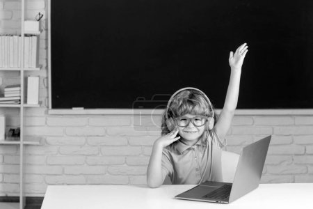 Téléchargez les photos : Mignon petit écolier garçon avec soulevé main étude dans un salle de classe - en image libre de droit