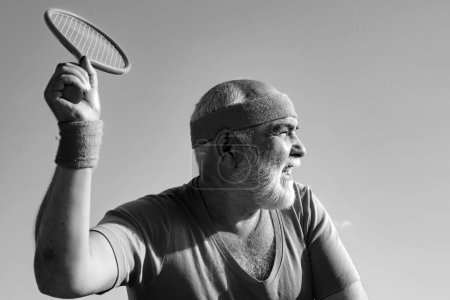 Photo for Elderly man practicing tennis on blue sky background. Senior man tennis player serving - Royalty Free Image