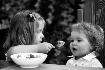 Téléchargez les photos : Frère nourricier. La fille nourrit bébé garçon avec une cuillère. Nourriture pour enfants. - en image libre de droit
