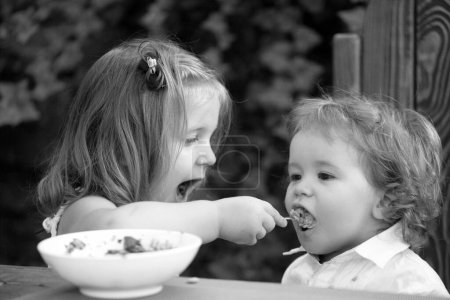Photo for Baby child eating food. Little girl sister feeds baby - Royalty Free Image